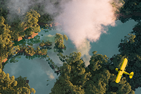 plane flying over a green space with water and steam rising up