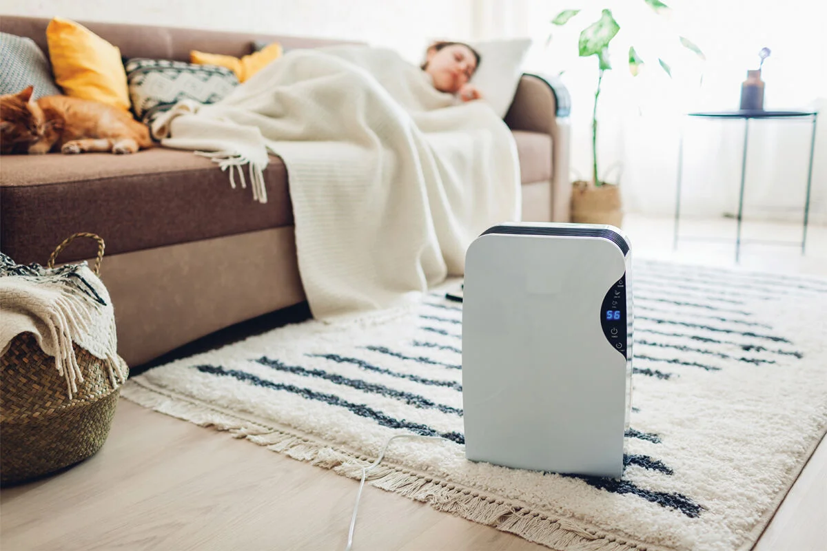 Person sleeping on the couch with an appliance running on the floor